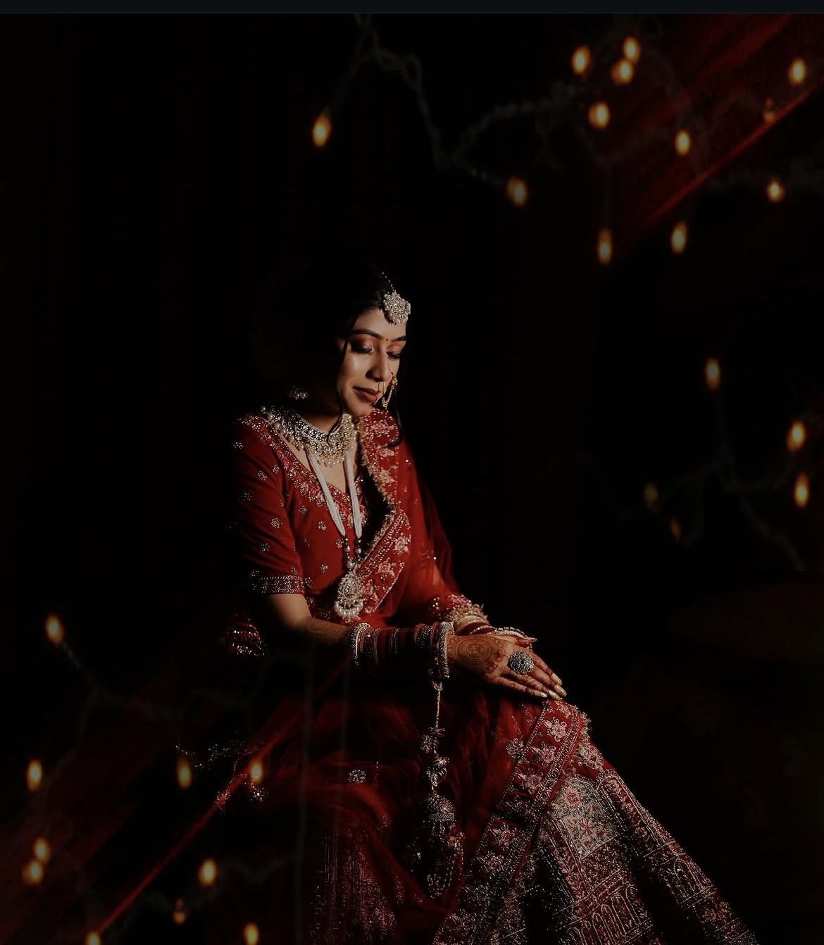 Bride seated beneath warm lights in a red wedding outfit